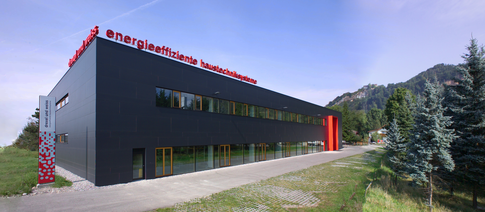 Modernes schwarzes Gebäude mit roter Beschilderung, umgeben von Grün und Bergen.