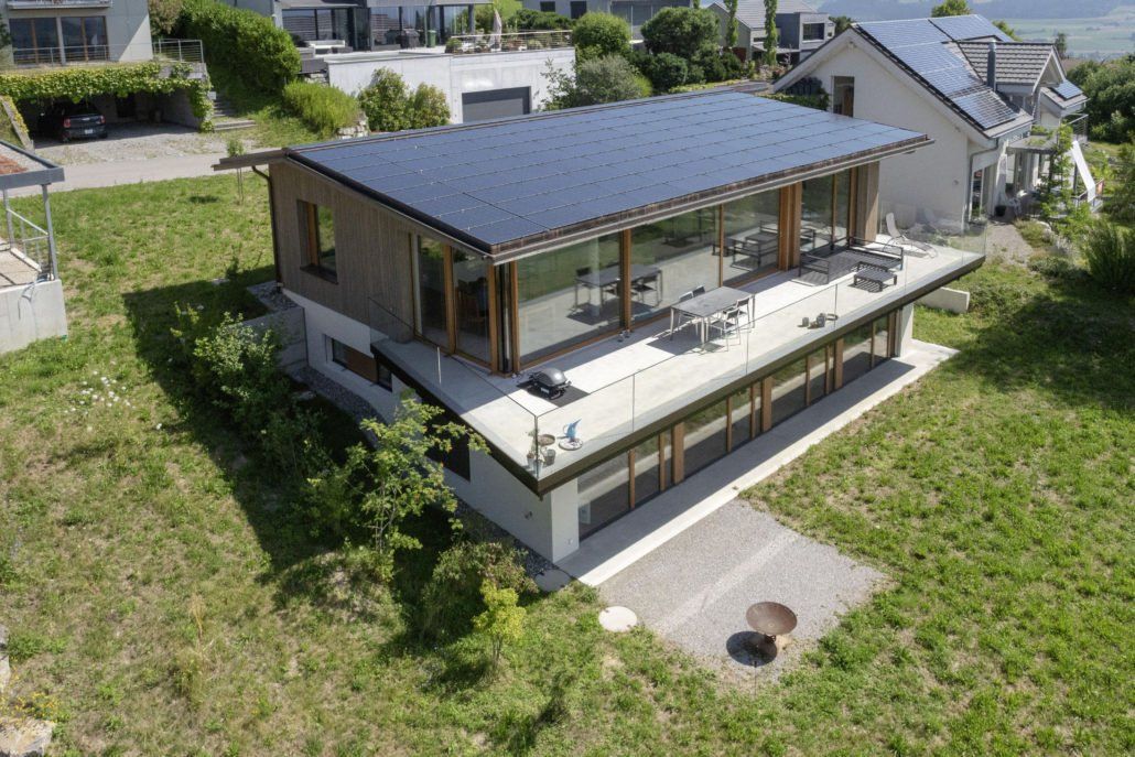 Modernes Haus mit Solaranlage am Hang, mit großen Fenstern und einem Sitzbereich im Freien.
