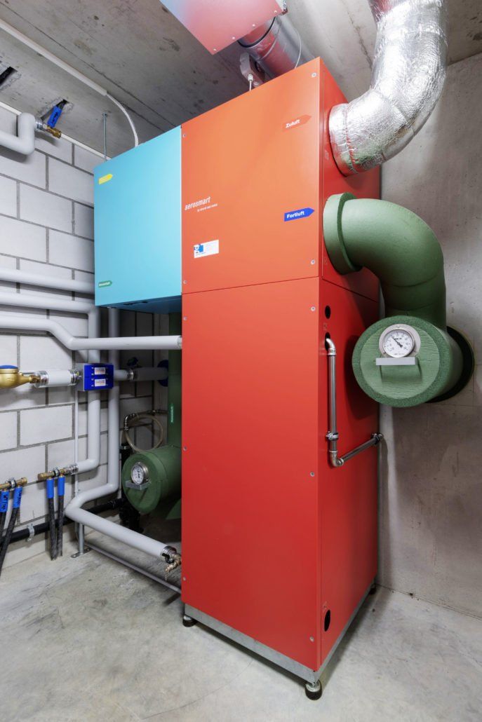Rote und blaue Klimaanlage mit grünen Rohren in einem Betonraum.