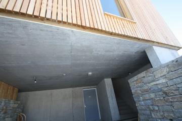 Außenansicht eines modernen Gebäudes mit Holzverkleidung auf einem Betonsockel und einer Steinmauer.