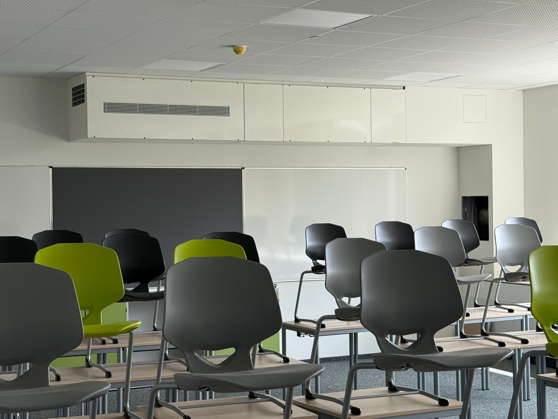 Klassenzimmer mit Stuhlreihen, einer Tafel und einer Projektionsfläche.