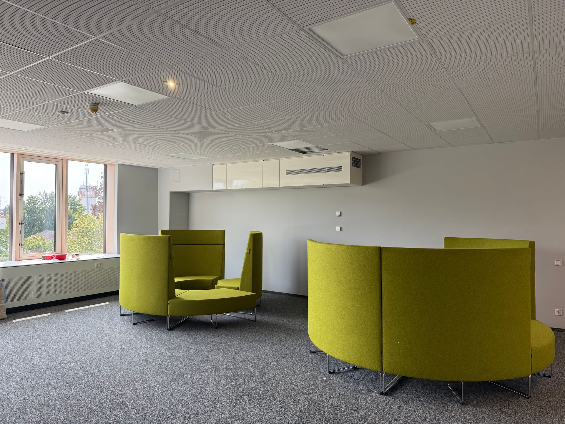 Moderne Büroräume mit limettengrünen modularen Sitzmöbeln und einer strukturierten Decke.
