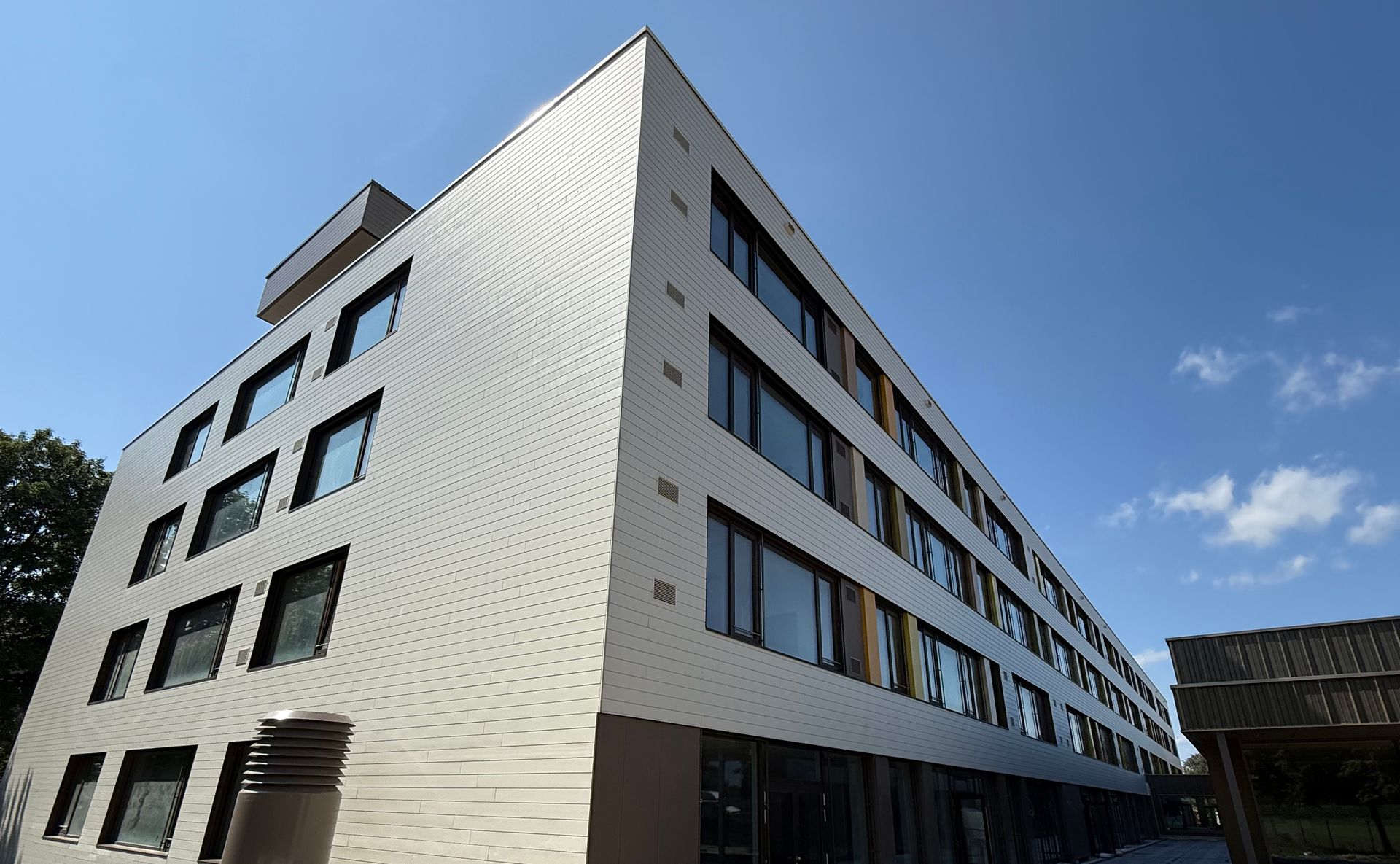 Modernes mehrstöckiges Gebäude mit weiß gemusterter Fassade vor blauem Himmel.