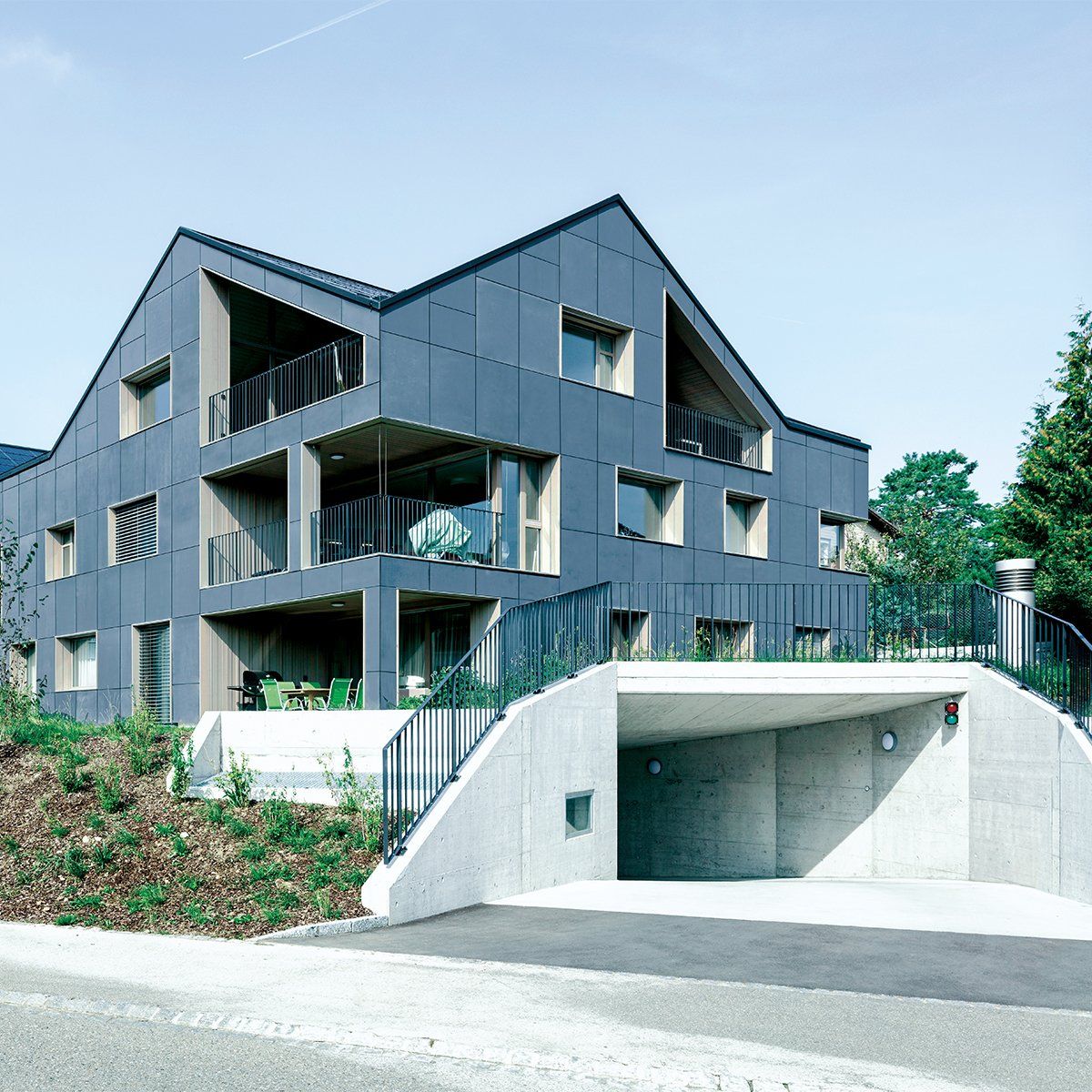 Modernes graues Mehrfamilienhaus mit Balkonen, Einfahrt und Schrägdach.