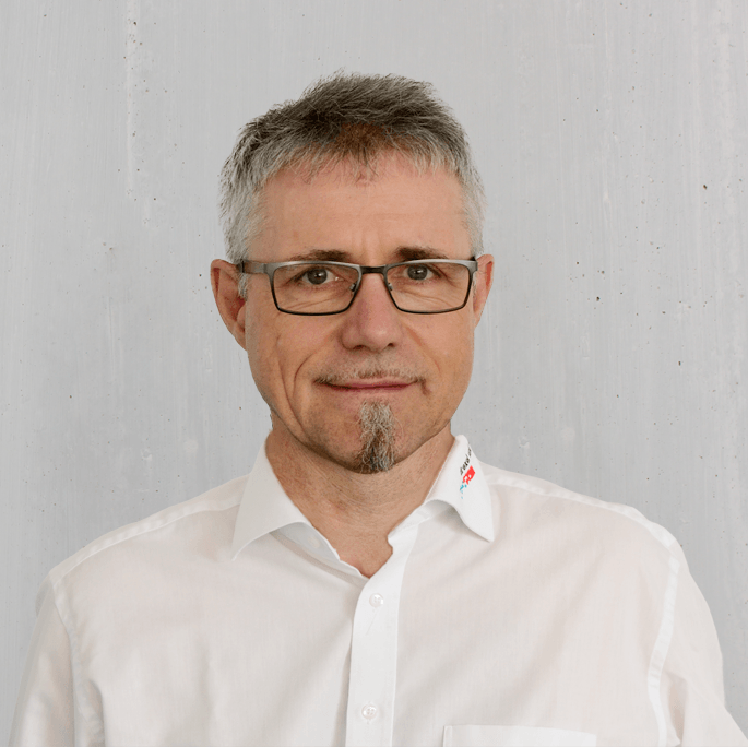 Mann mit Brille und weißem Hemd vor neutralem Hintergrund.