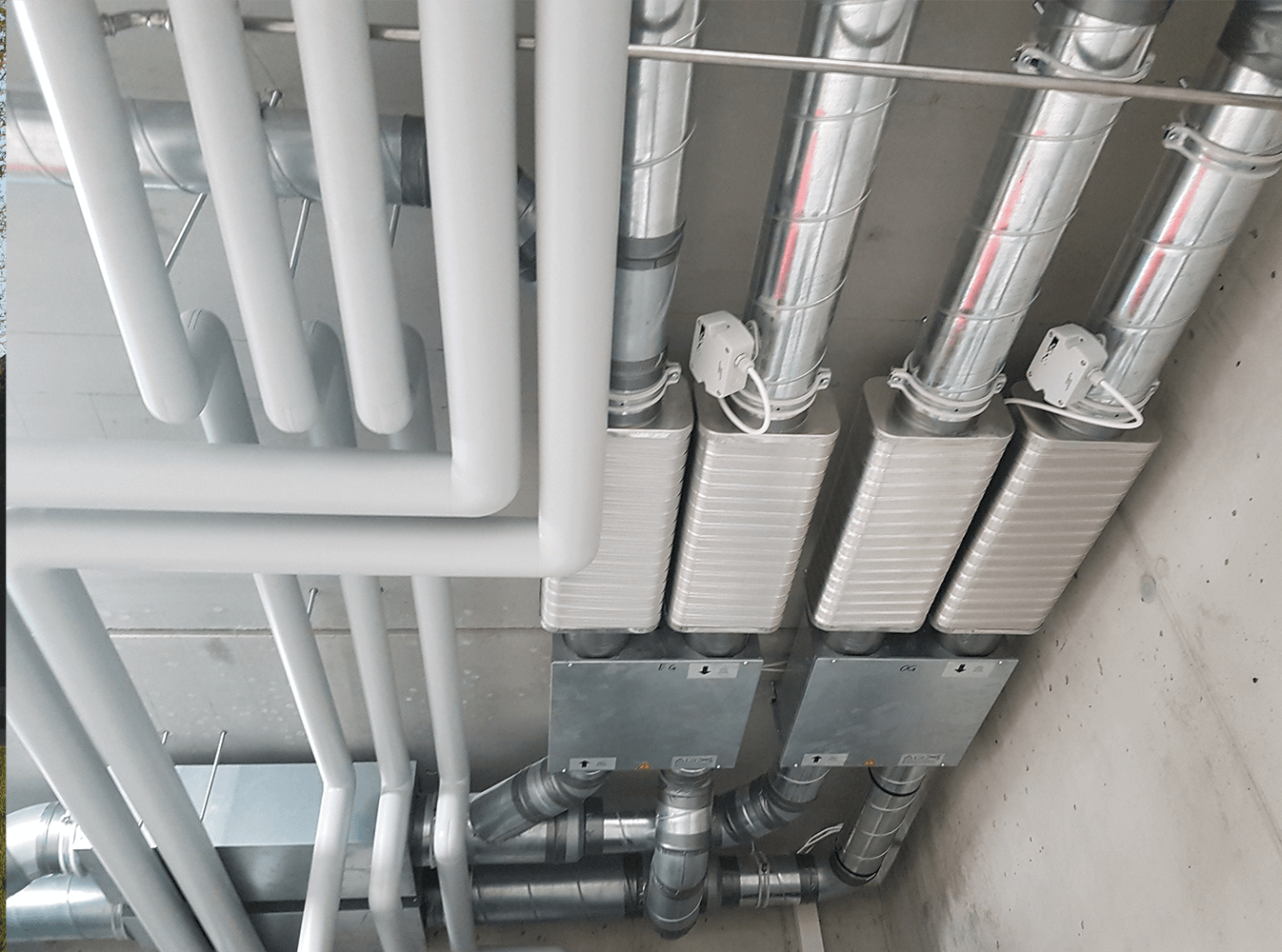 An der Decke befestigte Rohre und rechteckige Metallelemente, möglicherweise für ein Lüftungs- oder Klimaanlagensystem.