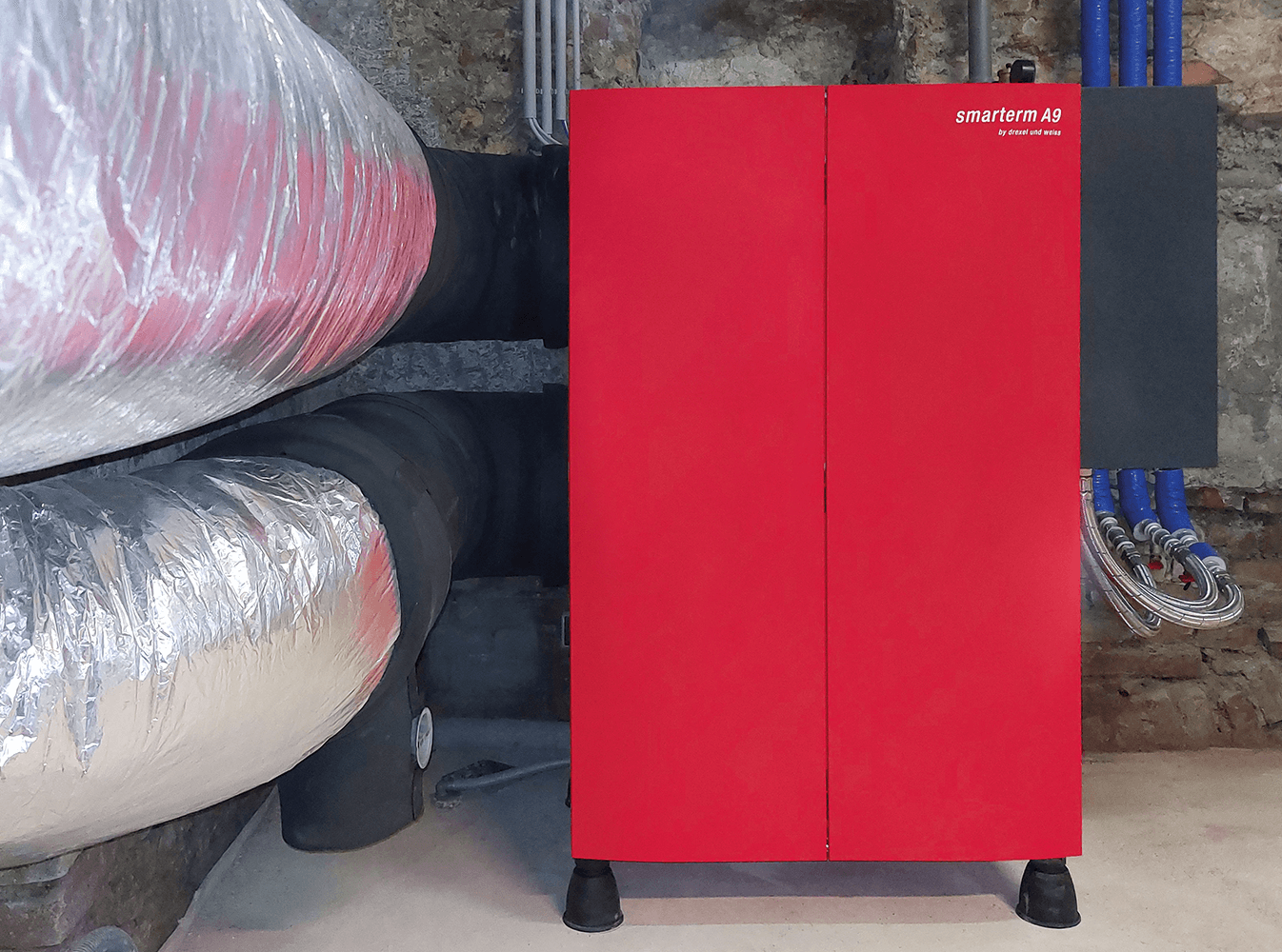 Ein roter Schrank mit der Aufschrift „revimer.it“ steht im Keller neben isolierten Rohren.
