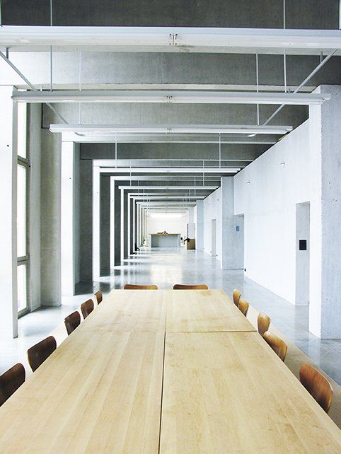 Langer, heller Flur mit einem Holztisch und Stühlen, beleuchtet von linearen Deckenleuchten.