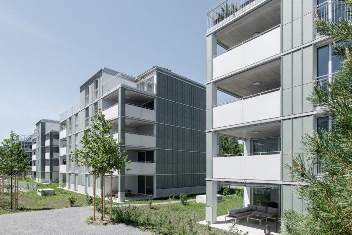 Moderne Wohnhäuser mit Balkonen und Metallverkleidung vor klarem Himmel.