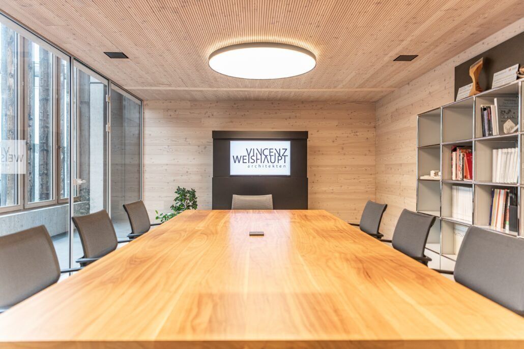 Moderner Konferenzraum mit großem Holztisch, Stühlen und Logo an der Wand.