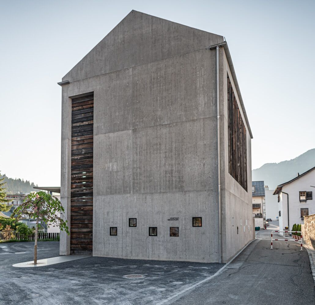 Graues Betongebäude mit Holzlatten, kleinen quadratischen Fenstern und einer großen Öffnung.