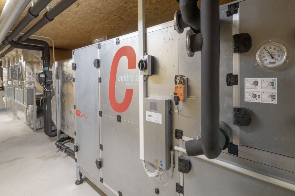 Große, industrielle Klimaanlage mit grauen Metallpaneelen, Rohrleitungen und Messgeräten; ein großes rotes „C“ ist sichtbar.
