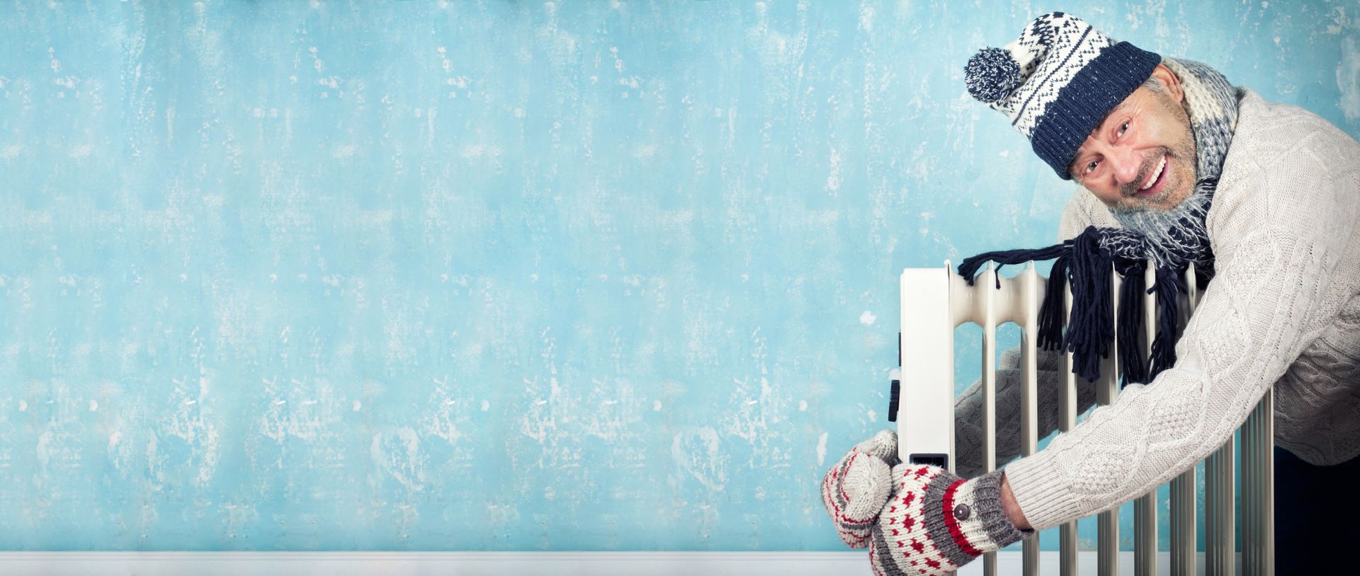 Eine Person in Winterkleidung lächelt und hält einen Heizkörper vor blauem Hintergrund.