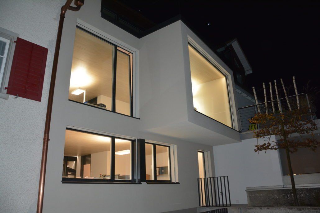 Modernes weißes Haus bei Nacht mit großen, beleuchteten Fenstern.