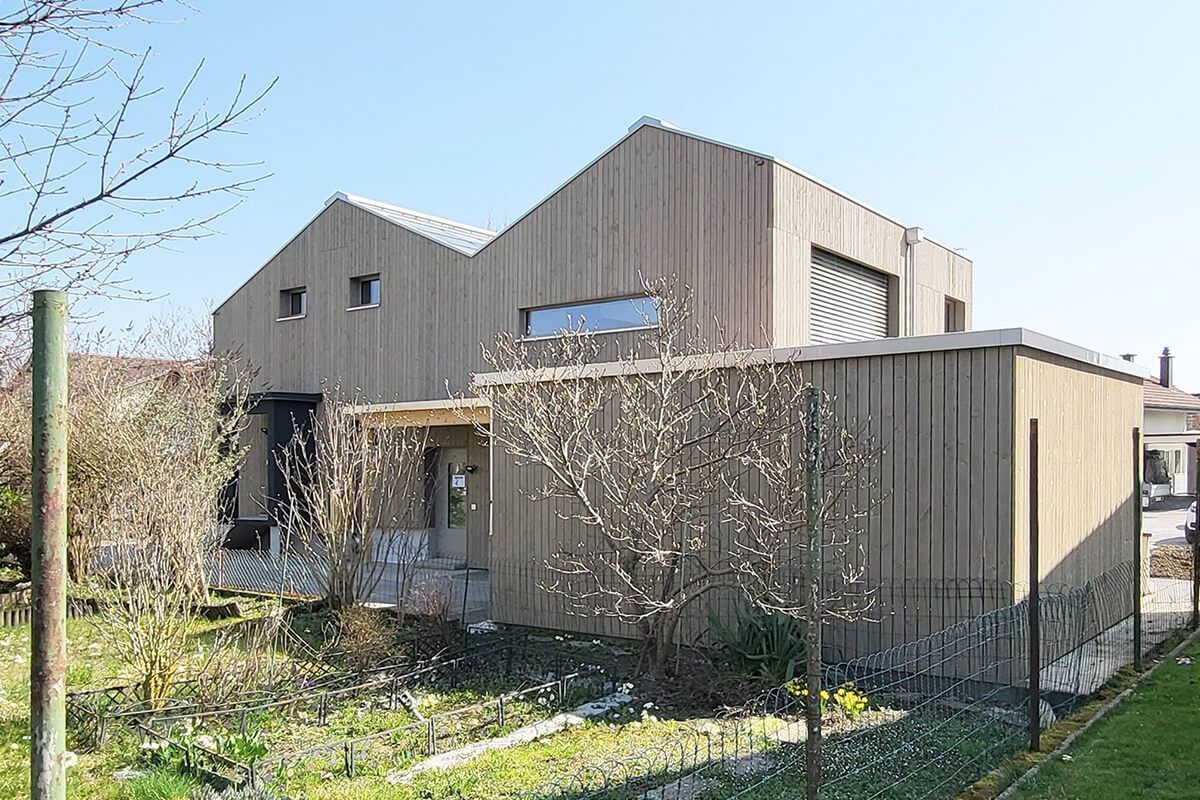 Modernes Holzhaus mit Giebeldach, überdachter Veranda und umzäuntem Hof.