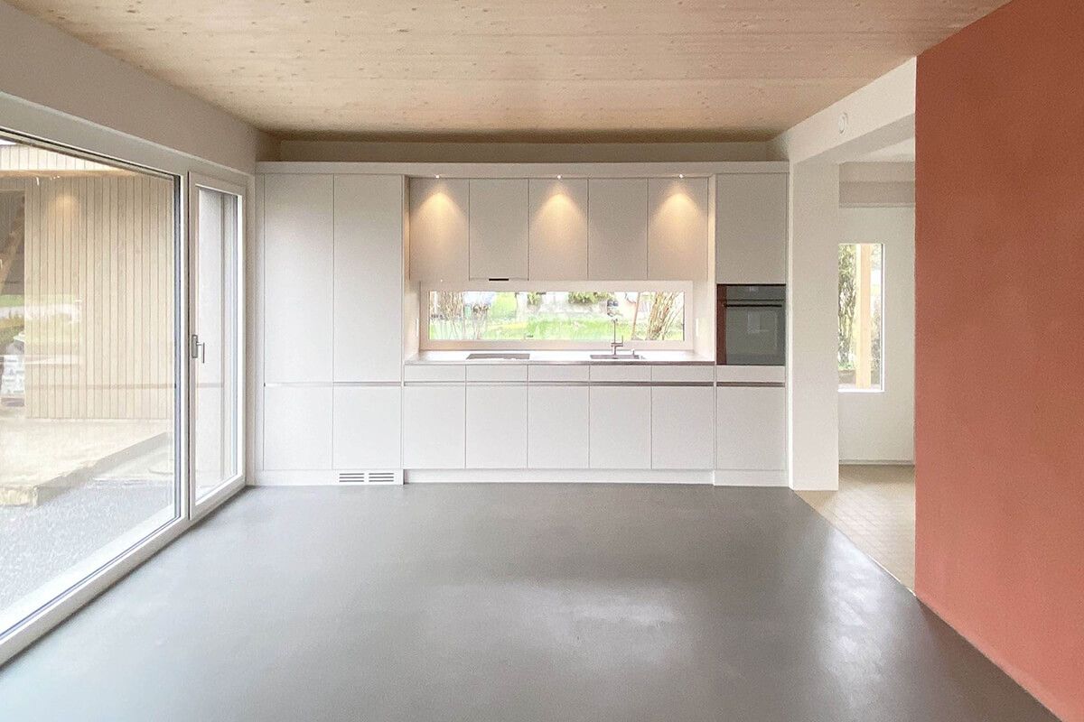 Moderne weiße Küche mit Glasschiebetüren, Betonboden und korallenfarbener Wand.