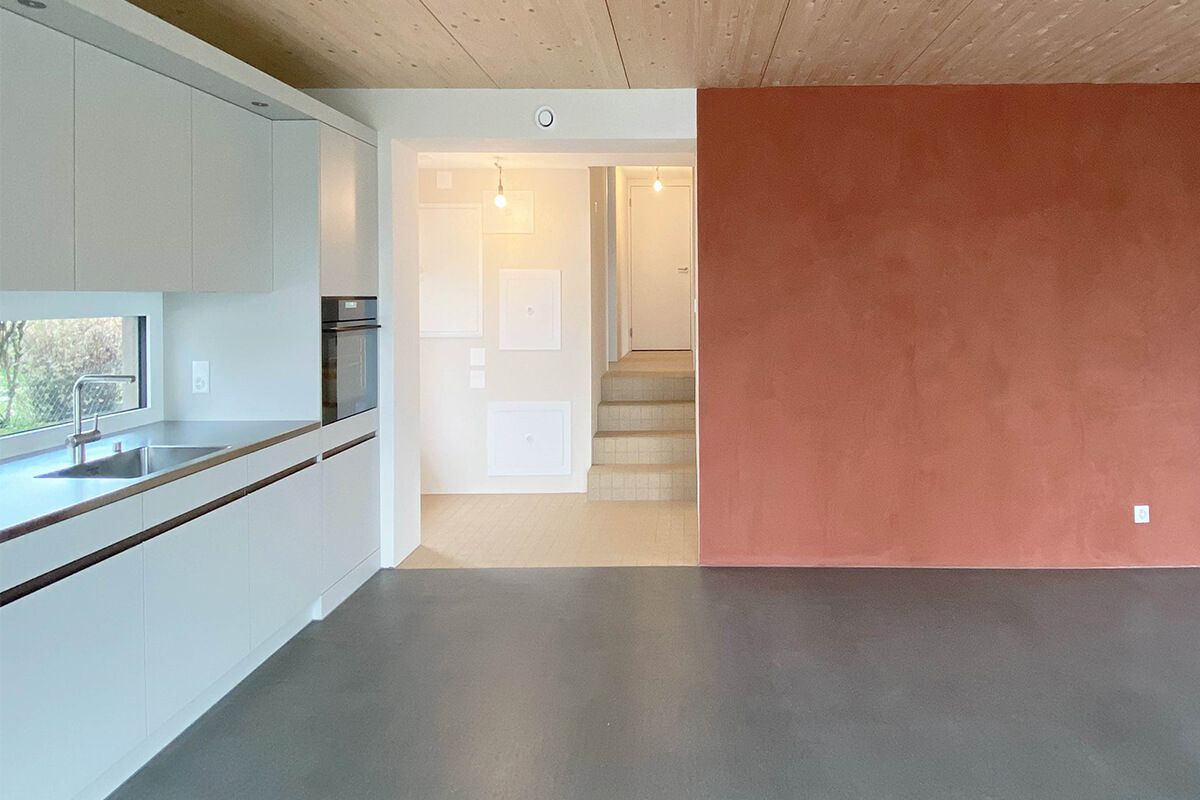 Modernes Interieur mit weißer Küche, roter Wand und Treppe, die nach oben führt.