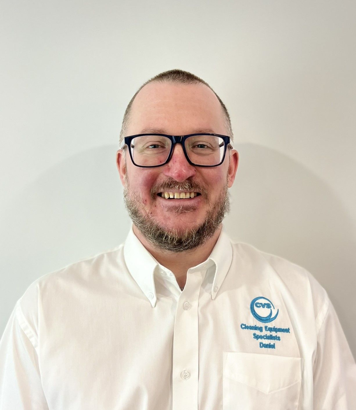 Man in white shirt with glasses smiles at the camera, logo on shirt.