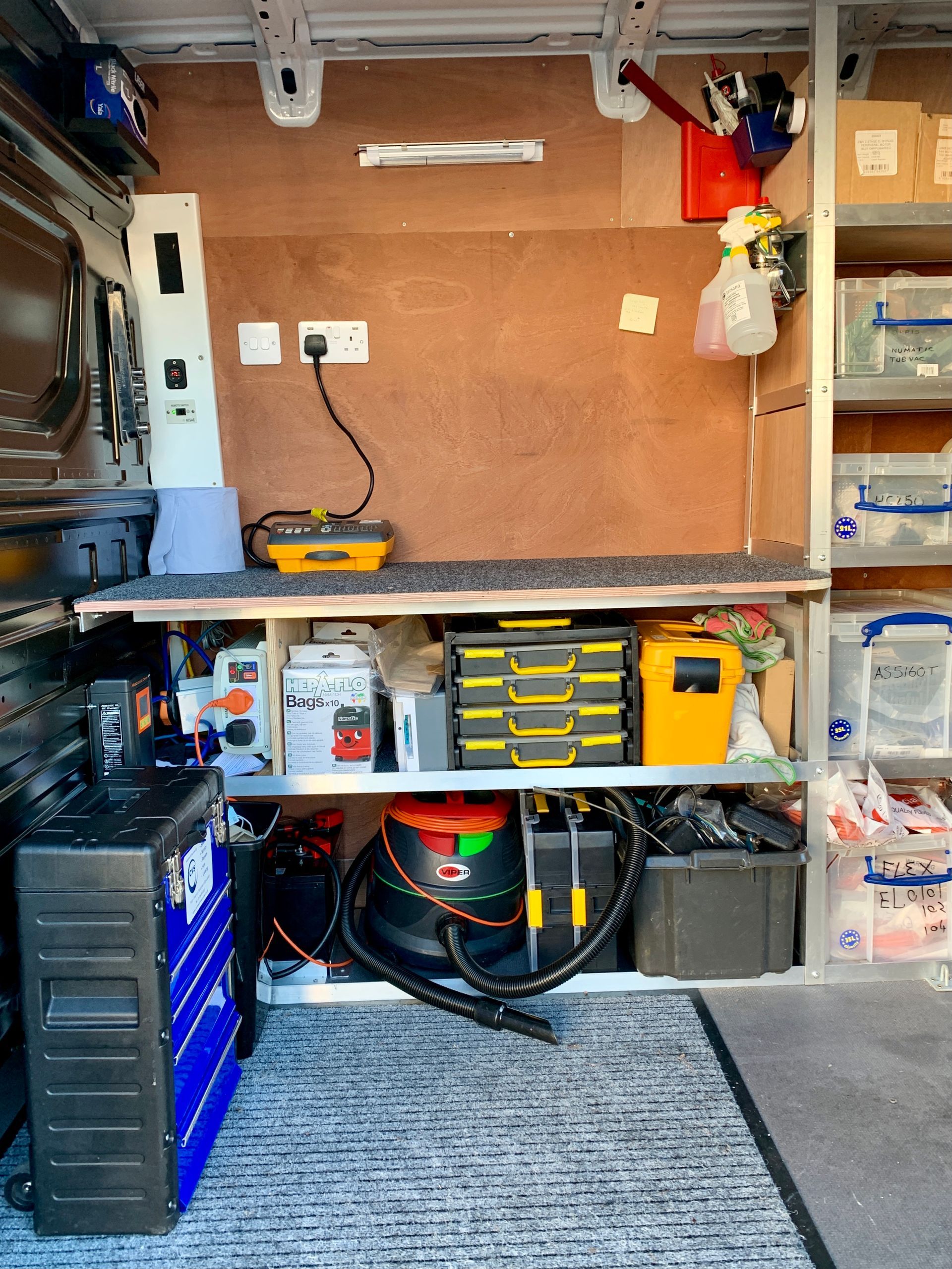 Interior of a van, organized work area with shelving, tools, electrical outlets, and a vacuum cleaner.