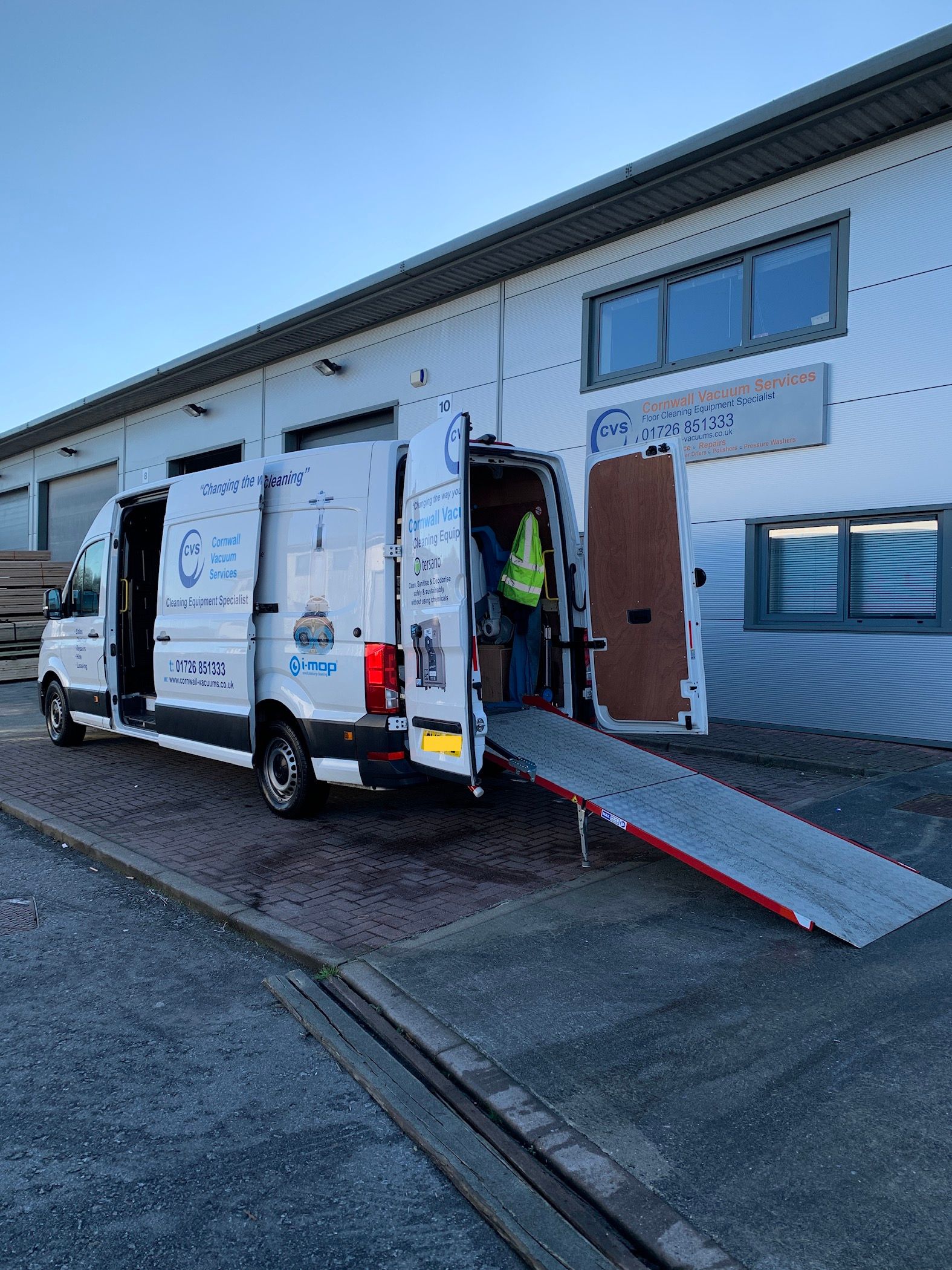 White van with ramp open, parked at a building. A person loads the van.