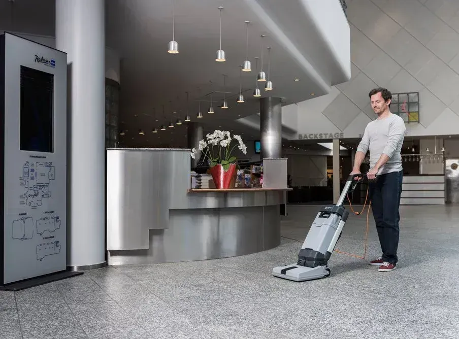 Upright commercial floor cleaner, gray and black, with orange cord.