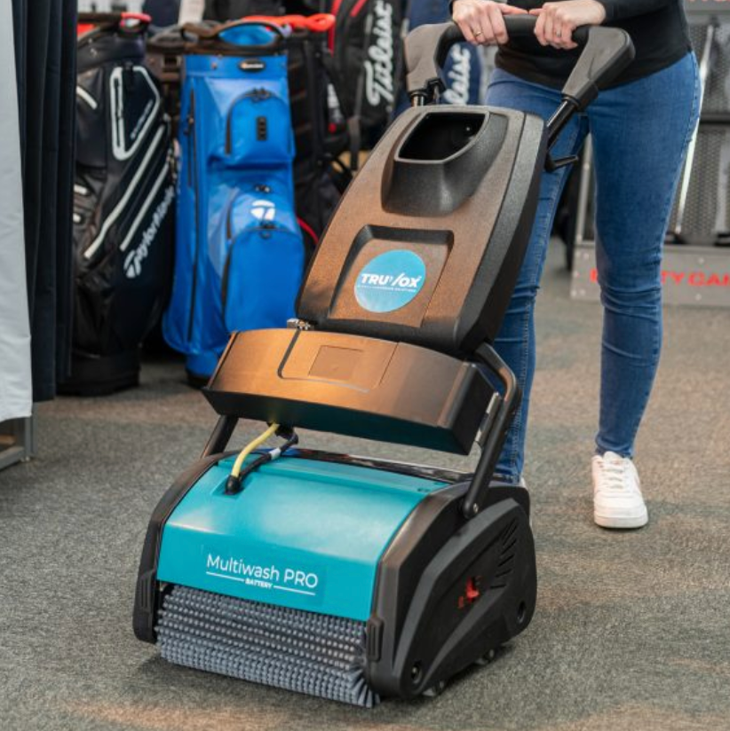 Person operating a teal and black floor cleaner labeled 