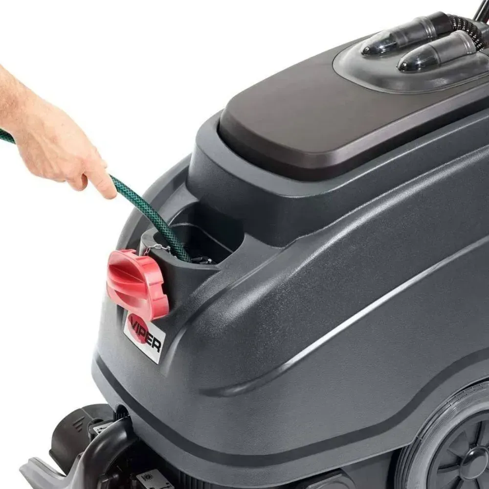 A person filling a dark gray floor cleaning machine with a green hose, near a red cap.