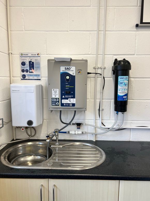 Sink with water filtration system, faucet, and dispenser mounted on a white brick wall.
