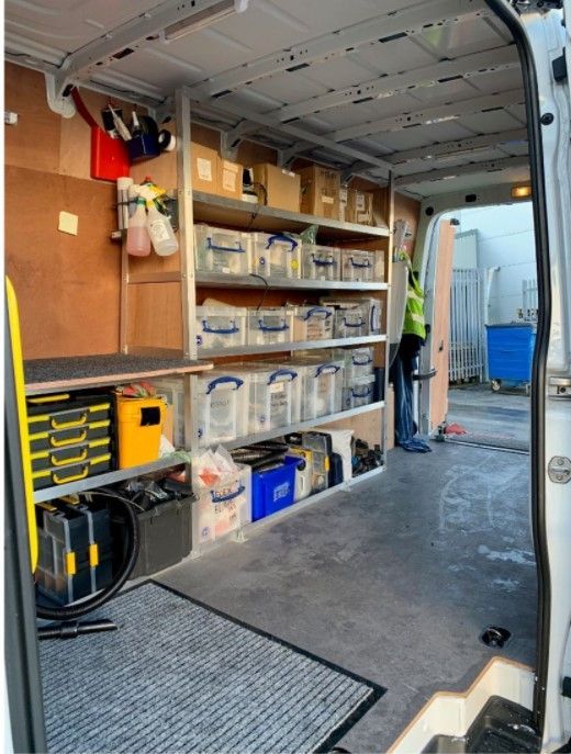 Interior of a white van with shelving, storage boxes, tools, and a person.