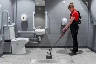 Person cleaning a public restroom floor with a scrubber.