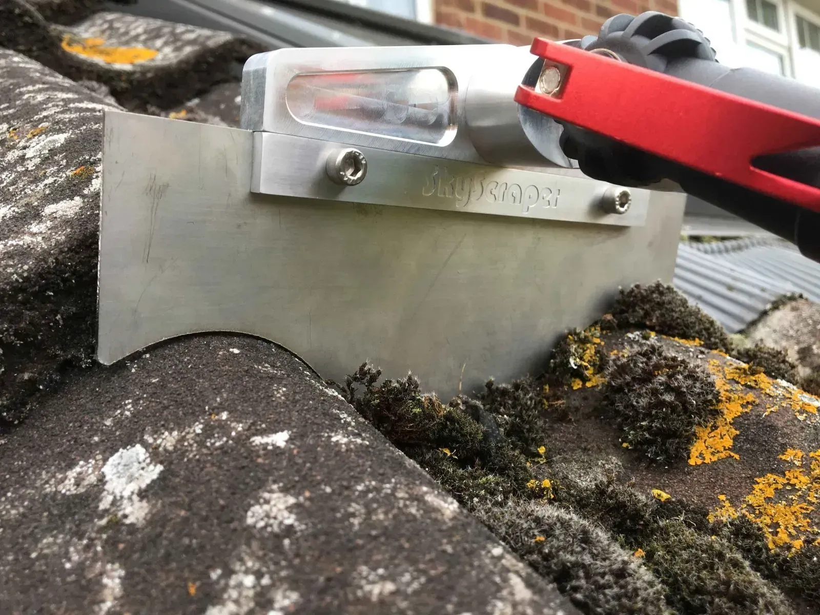 A roofing tool with a metal blade removing moss from weathered tiles on a roof.