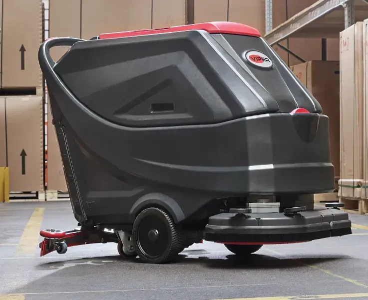 Floor cleaning machine in a warehouse. Gray and red machine on concrete floor with boxes in the background.