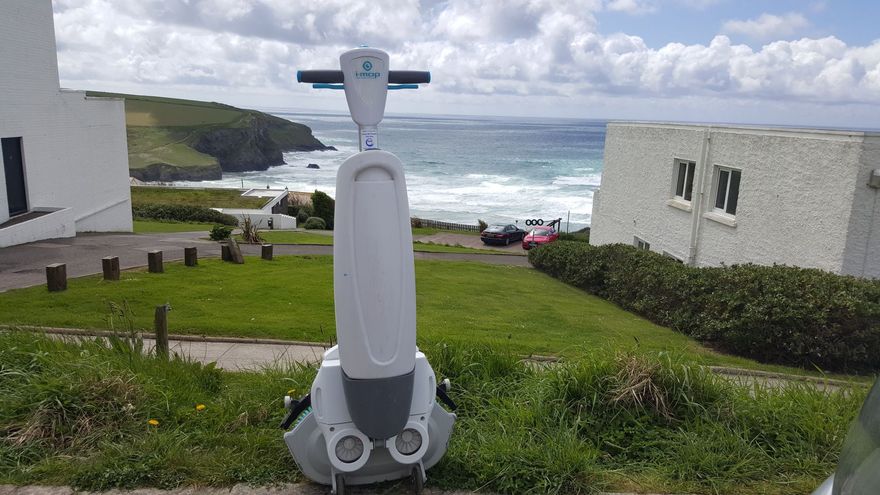 A white robot on a grassy hill overlooking the ocean. The sky is cloudy.