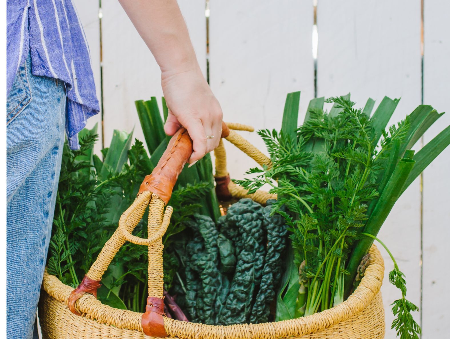 A person is holding a basket full of vegetables.
