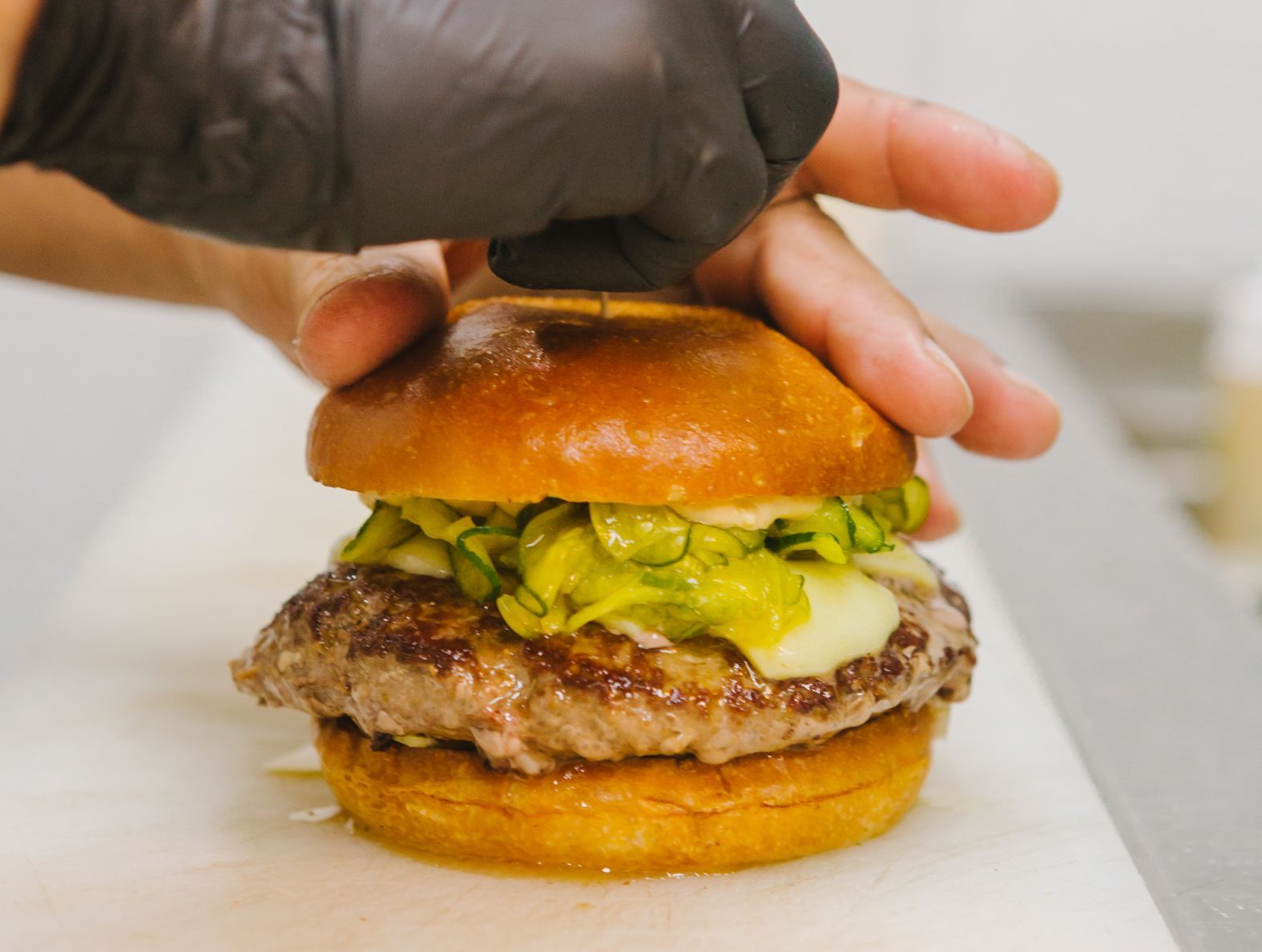 A person wearing black gloves is holding a hamburger on a bun.