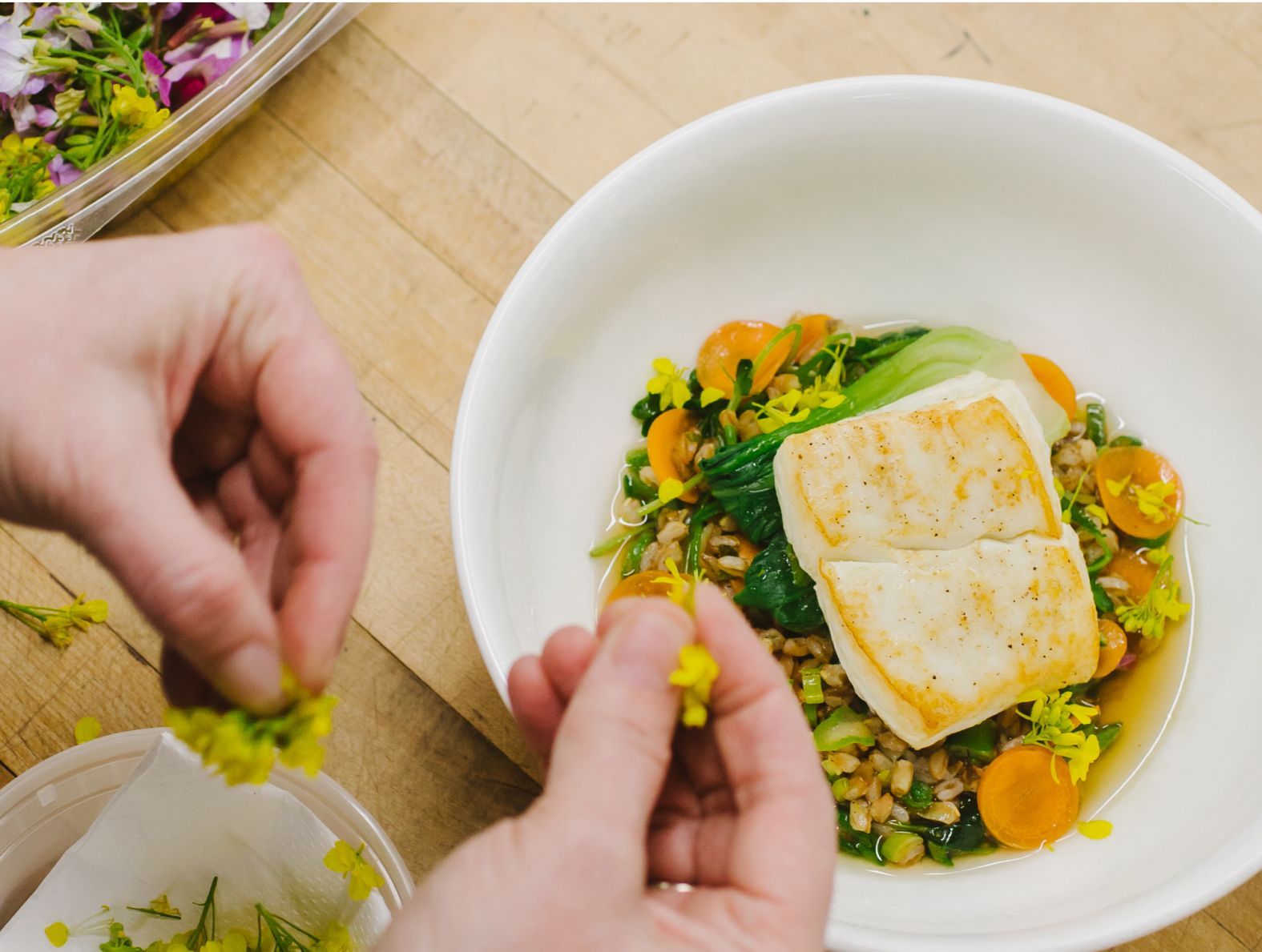 A person is adding flowers to a bowl of food.