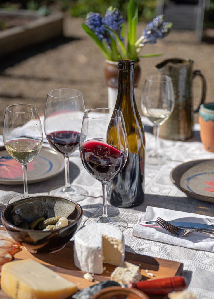 A table topped with a bottle of wine , glasses of wine , cheese , and flowers.