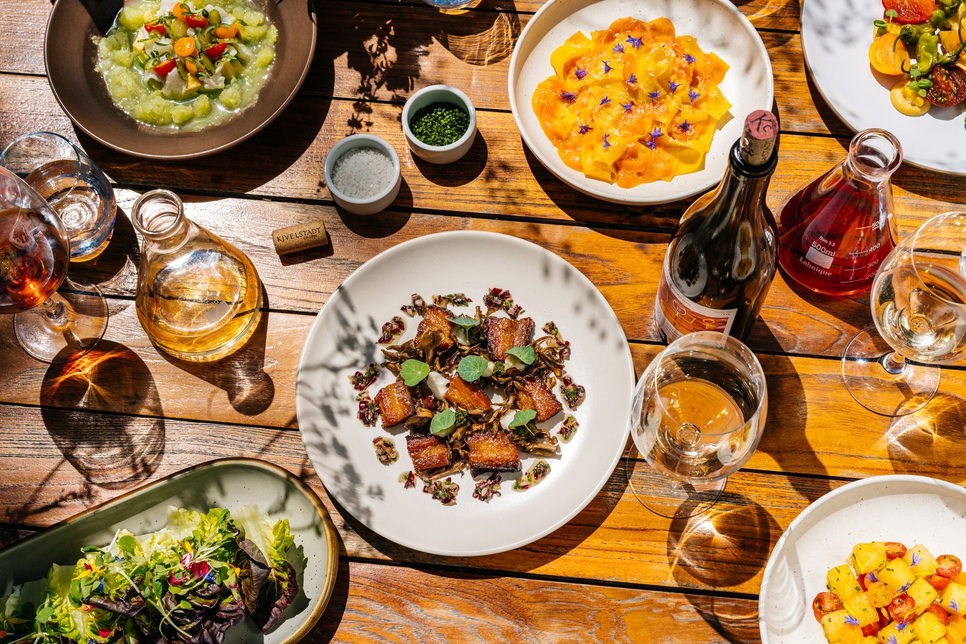 A wooden table topped with plates of food and wine glasses.
