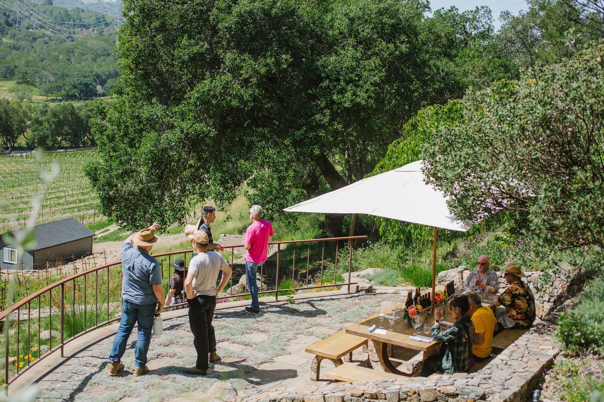 A group of people are standing around a picnic table under an umbrella.