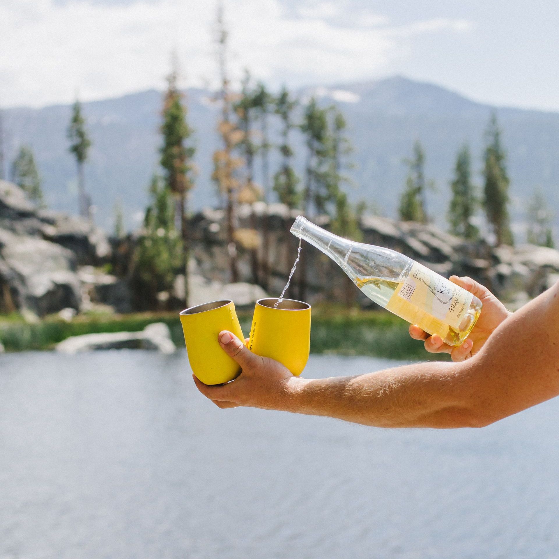 A person is pouring water from a bottle into a yellow cup.