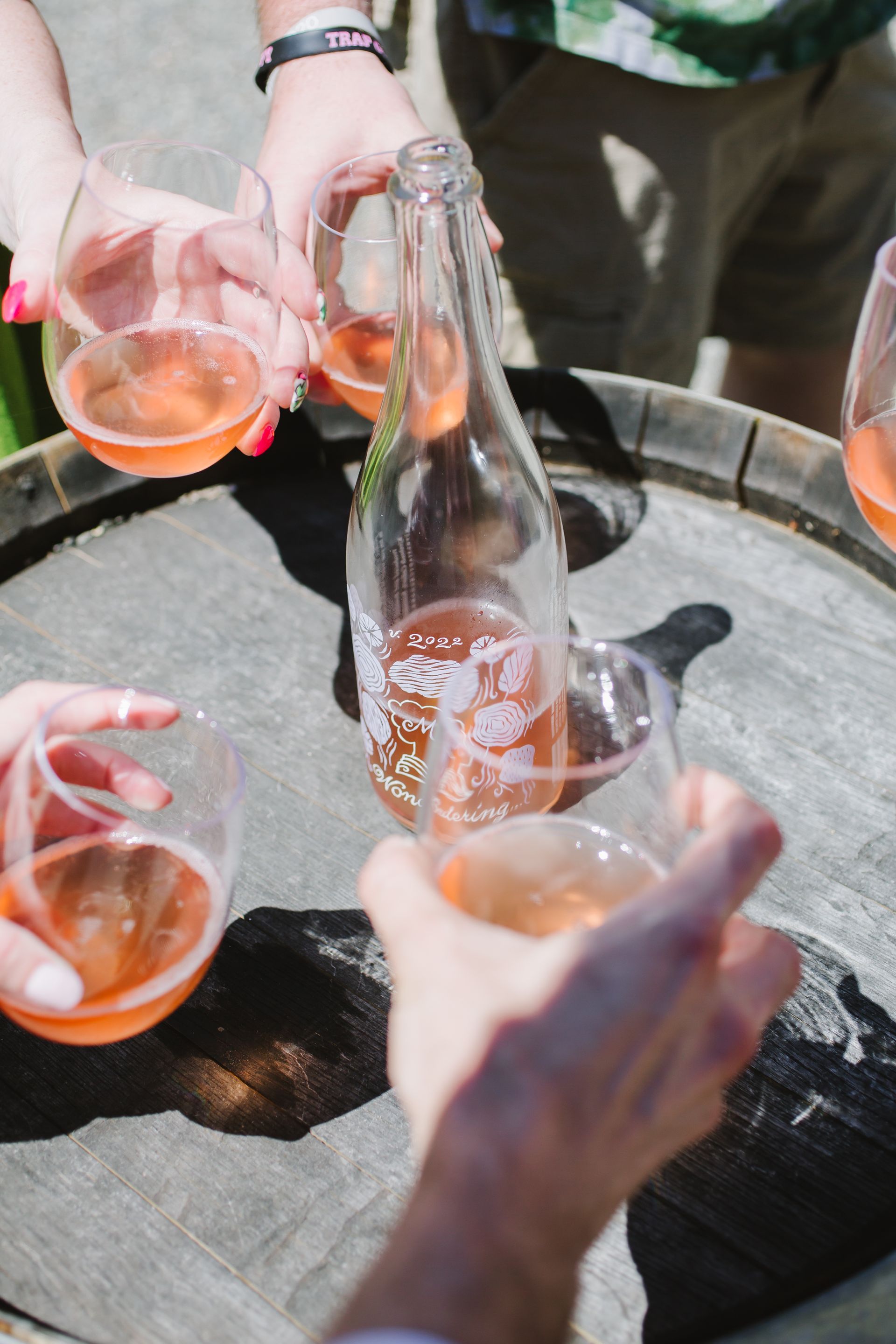 A group of people are toasting with wine glasses and bottles on a barrel.