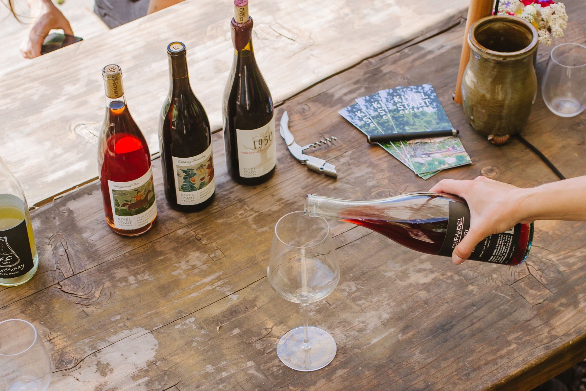 A person is pouring wine into a glass on a wooden table.