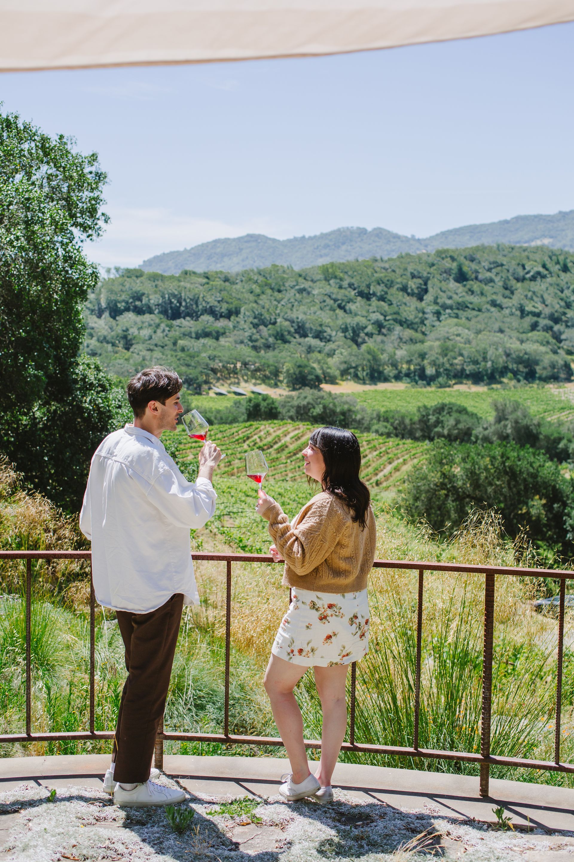 A man and a woman are standing on a balcony drinking wine.
