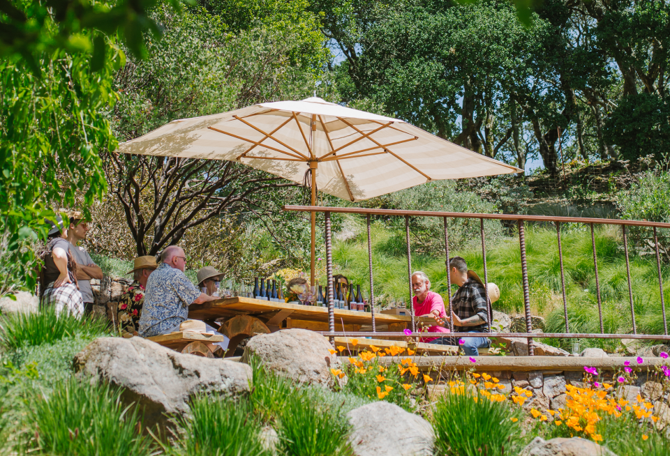 A group of people are sitting at a picnic table under umbrellas.