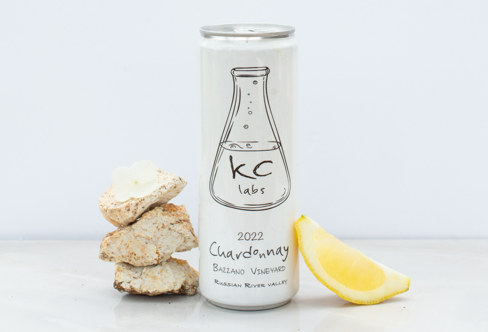 A can of chardonnay wine is sitting on a table next to a slice of lemon.
