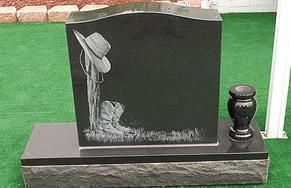 Black gravestone with engraved cowboy and horse beside a small urn on a grass lawn