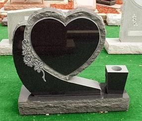 Heart-shaped black granite memorial with floral carving and candle holder on a base outdoors
