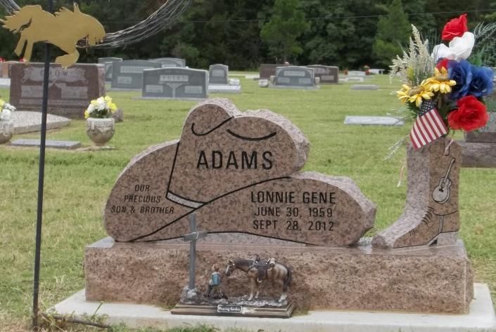 Decorated cemetery headstone with “ADAMS” and flowers, including a small American flag and military tribute.