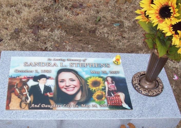 Memorial plaque with smiling woman’s photo and sunflowers on a stone grave marker beside a vase