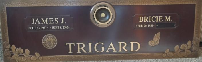 Maroon memorial plaque with gold lettering for James J. and Bricie M. Trigard, framed by floral accents
